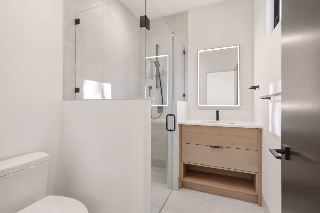 Bathroom in this Osoyoos custom home with a glass shower, backlit mirror, and light wood vanity with black fixtures.
