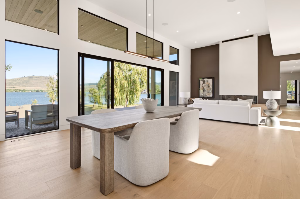 Dining table and lake view through floor-to-ceiling glass in this Osoyoos custom home with wide-plank wood floors.
