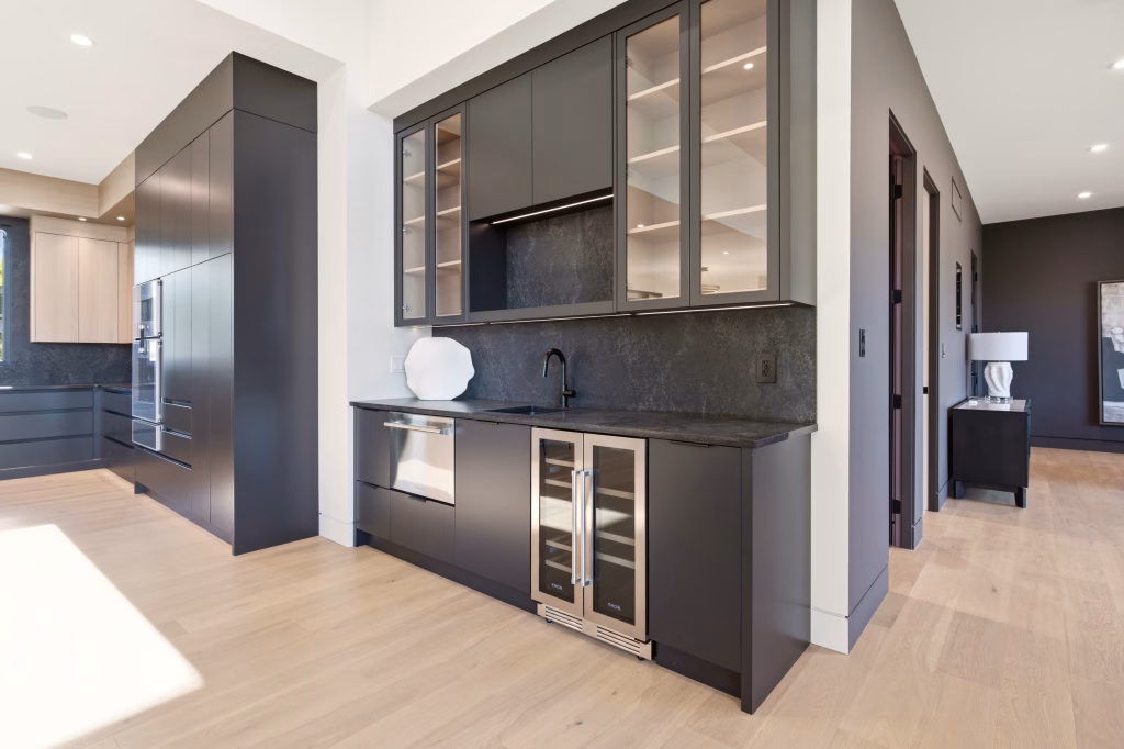 Wet bar with stone backsplash, glass-front display cabinets and a beverage fridge in this Osoyoos custom home.