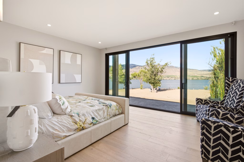 Bedroom with sliding glass doors opening to the private sandy beach at this Osoyoos lakefront home.