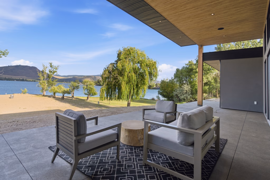 Covered patio with a wood-lined ceiling and lounge seating overlooking the lake at this Osoyoos lakefront home.